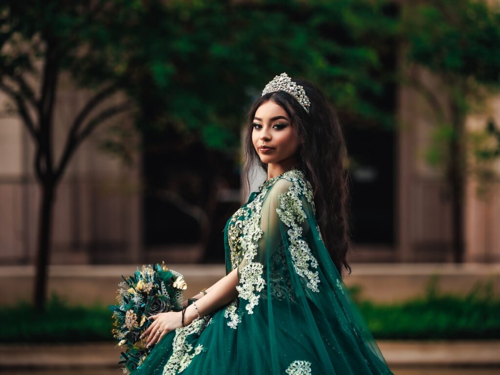 Quinceanera close-up in emerald cape dress near urban water feature, moody portrait taken on a rainy day in downtown Indianapolis.