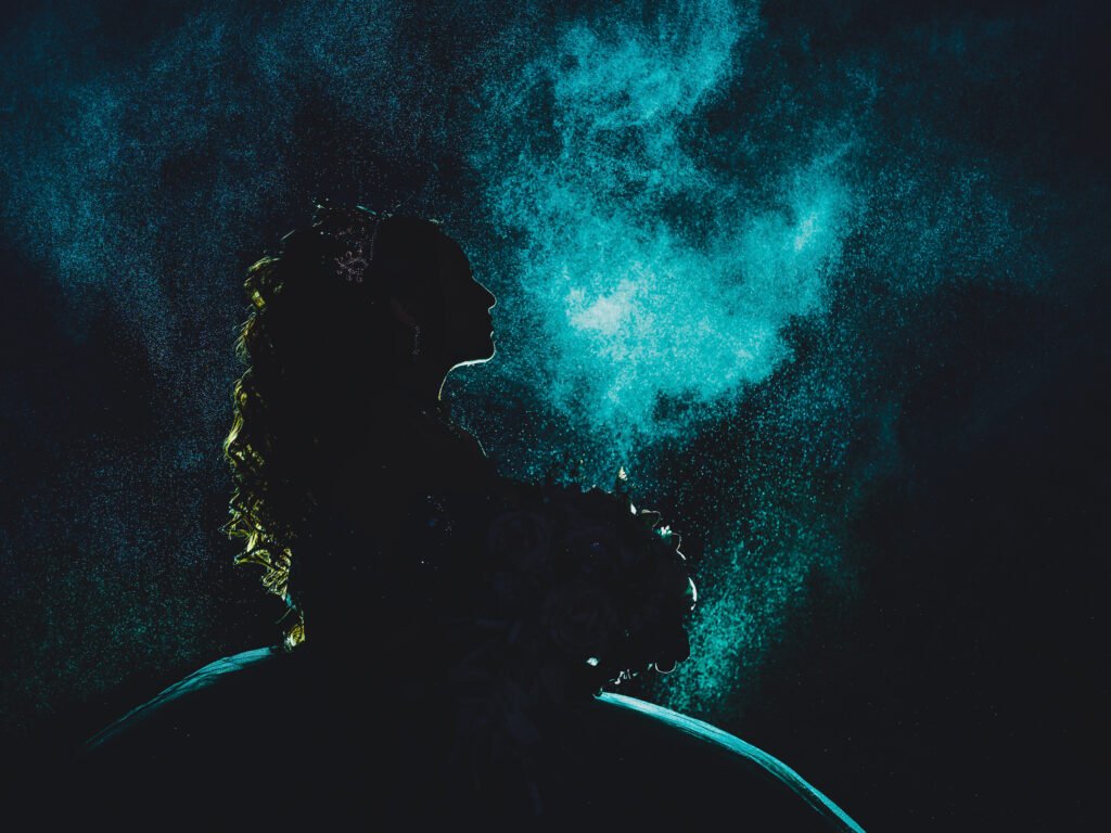 Quinceanera silhouette profile with dramatic blue backlighting and particle effects, moody cinematic portrait at Coxhall Gardens.