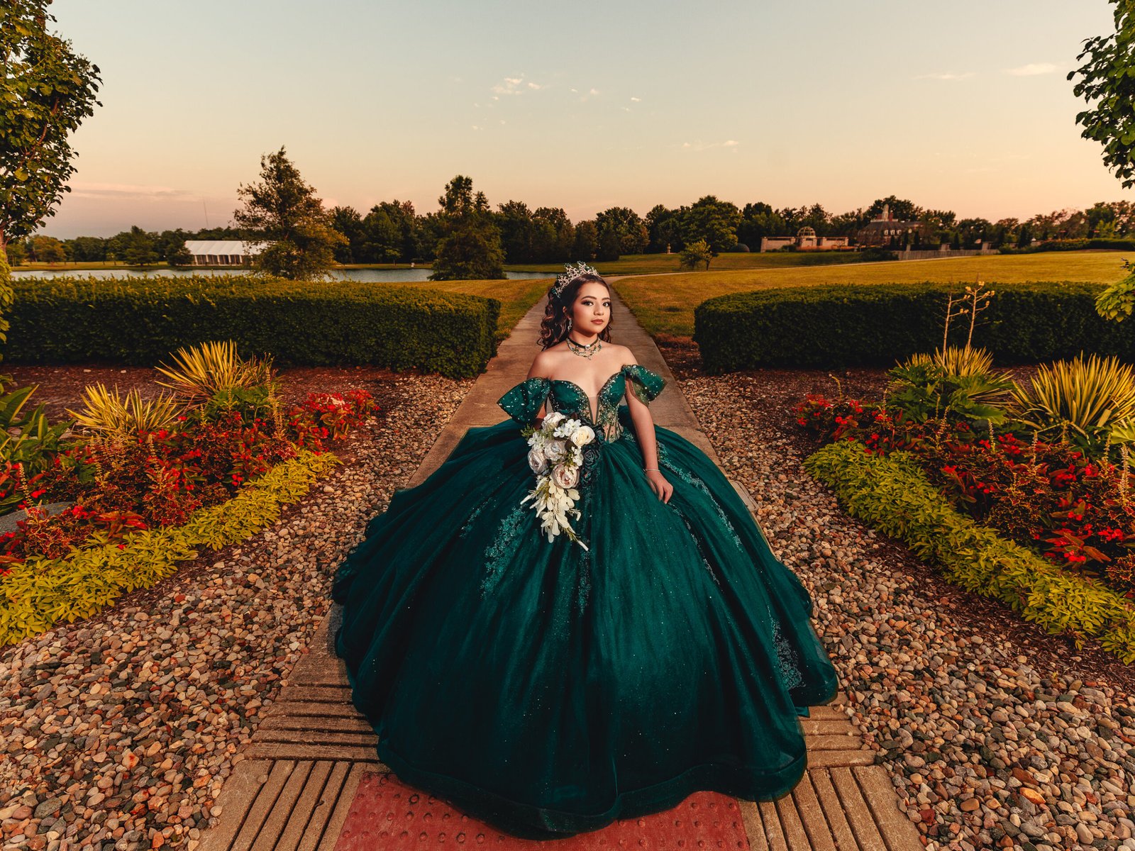 Quinceanera standing on garden path in emerald dress, cinematic golden hour lighting and fine art style at Coxhall Gardens.