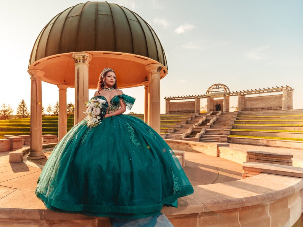 Quinceanera in emerald dress standing under the stone dome at Coxhall Gardens, wide angle cinematic sunset shot.