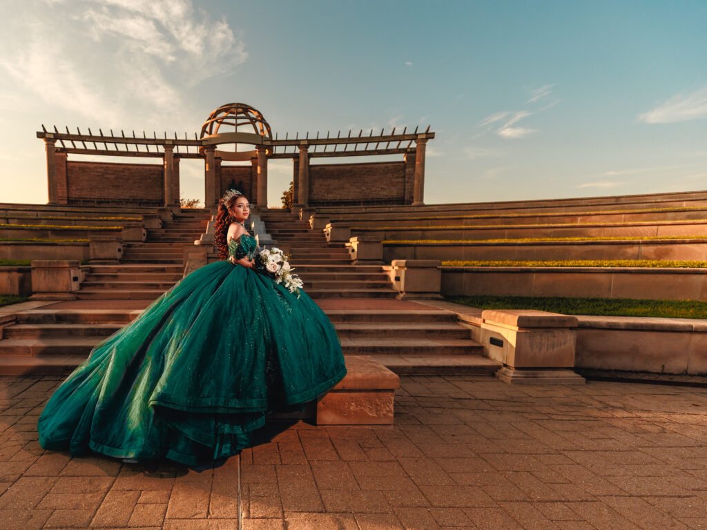Quinceanera in emerald dress posing under the stone dome at Coxhall Gardens, cinematic wide-angle sunset portrait.