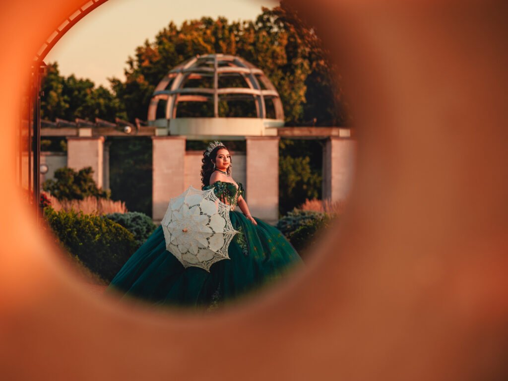 Quinceanera standing on garden path in emerald gown, cinematic sunset lighting and fine art aesthetic at Coxhall Gardens.