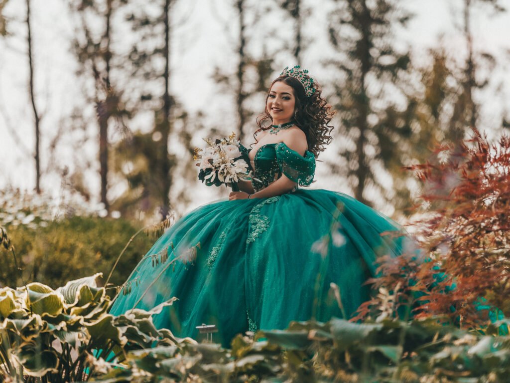 Smiling Quinceanera holding bouquet in green gown, fine art atmospheric portrait at Coxhall Gardens.