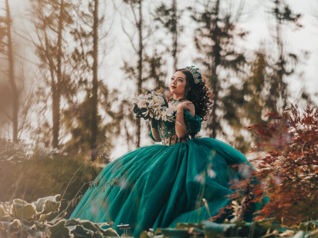 Smiling Quinceanera holding bouquet in green gown, fine art atmospheric portrait at Coxhall Gardens.