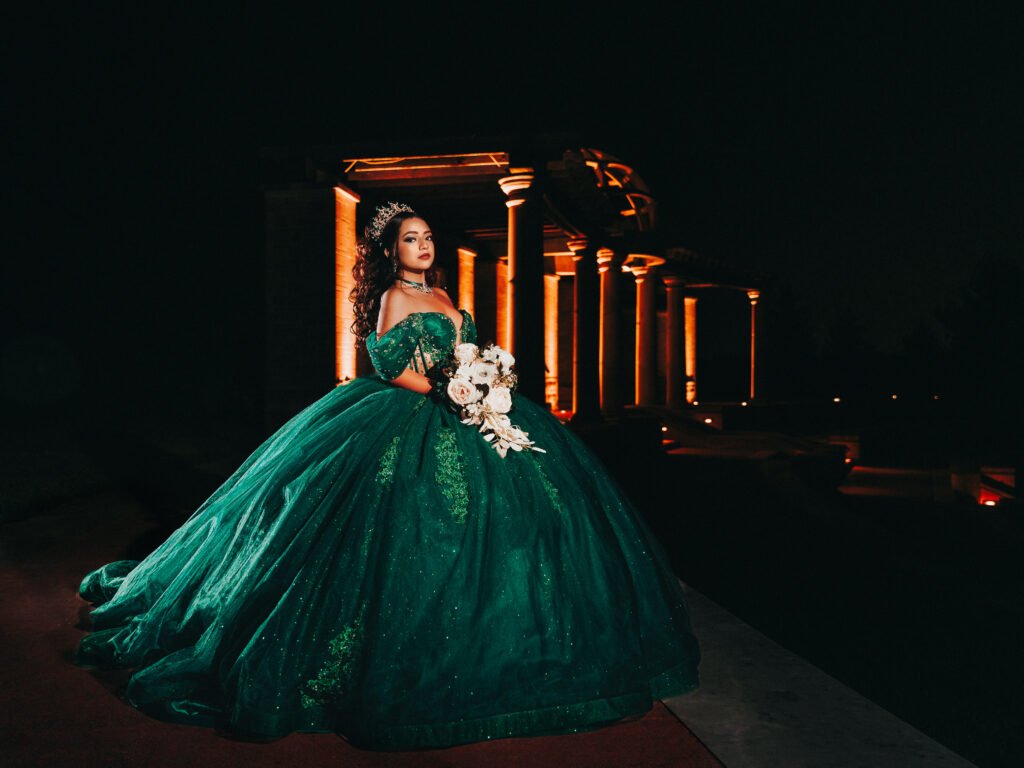 Dramatic portrait of Quinceanera in green dress with bouquet, moody architectural lighting and cinematic style.