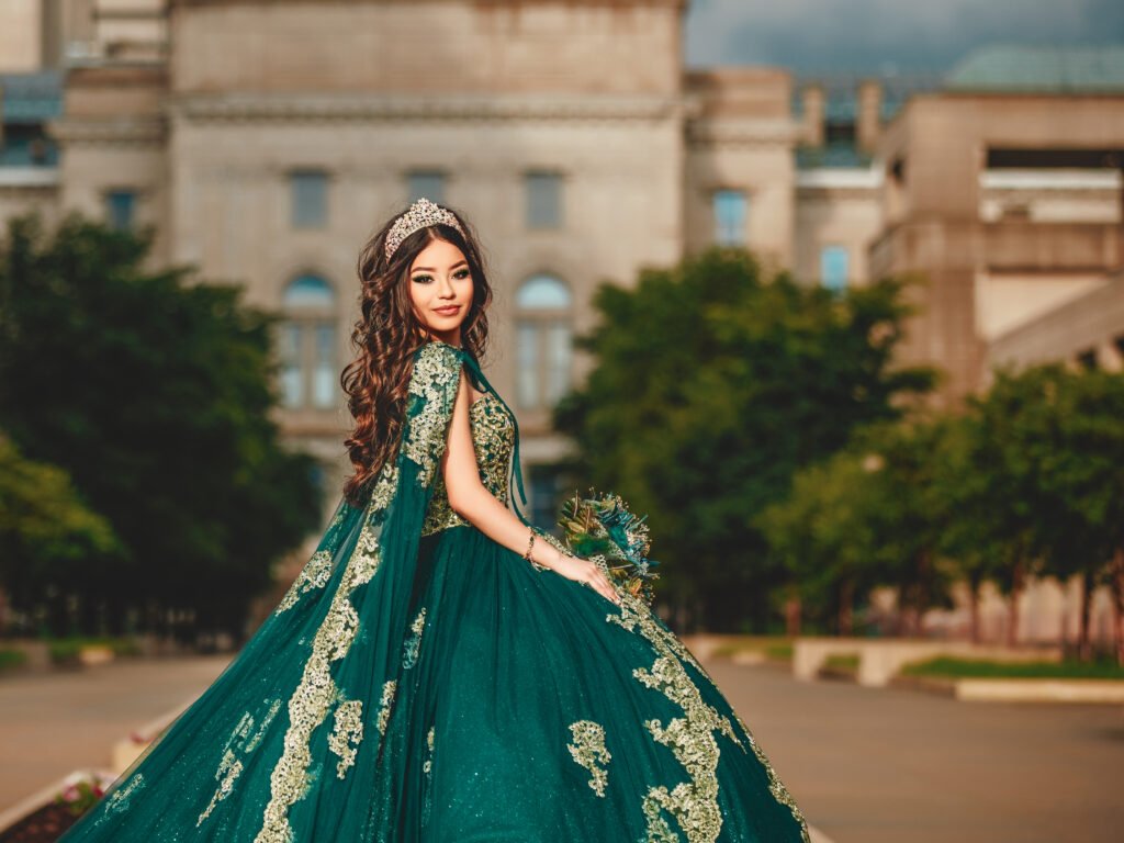 Captivating wide-angle shot of a Quinceañera in an Emerald Green Quinceañera Dress with a long train, featuring the Indiana State House in the background.