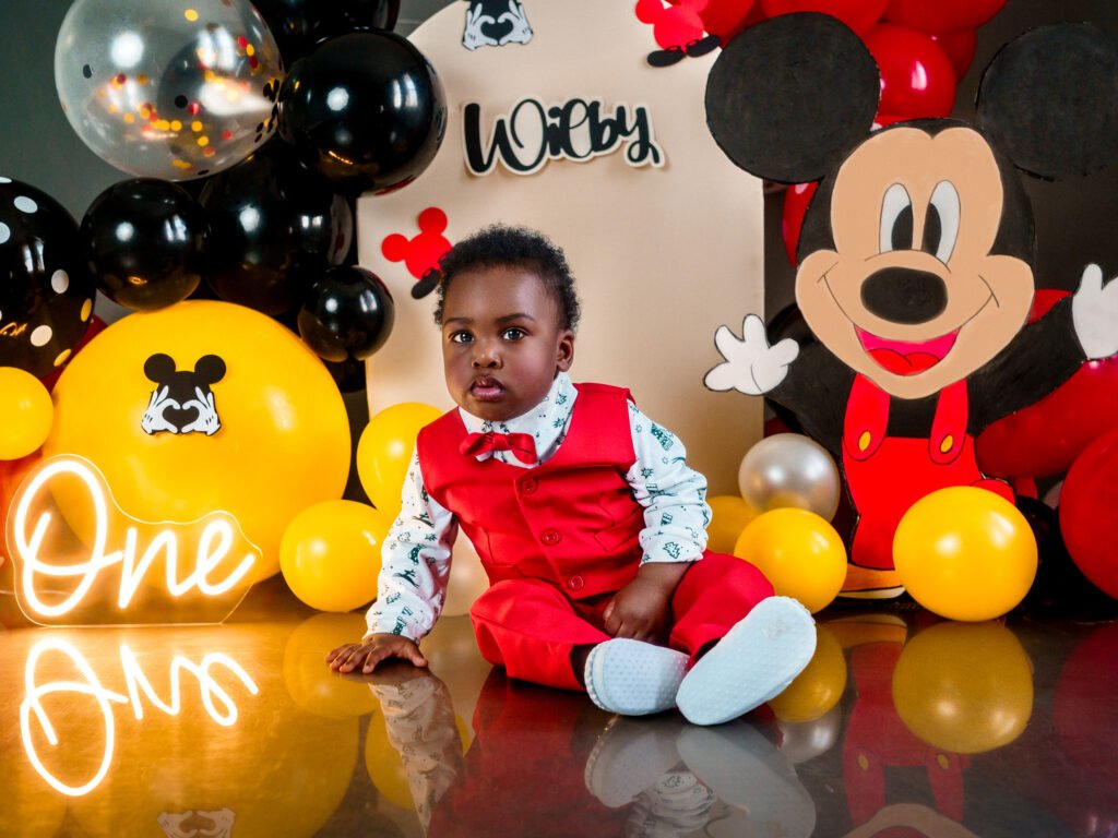 Toddler with Mickey Mouse birthday cake and custom balloon arch, professional studio set in Indianapolis