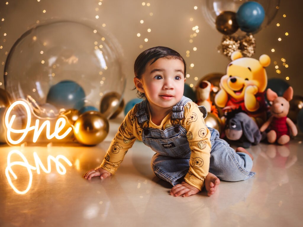 Horizontal Fine Art Indianapolis Cake Smash set with Winnie the Pooh, LED "One" sign, and giant transparent balloons.