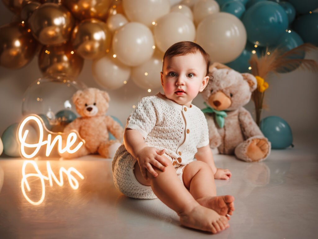 Baby boy in a cream knitted romper and light blue bowtie smiling while sitting in his custom Fine Art Indianapolis Cake Smash studio set.