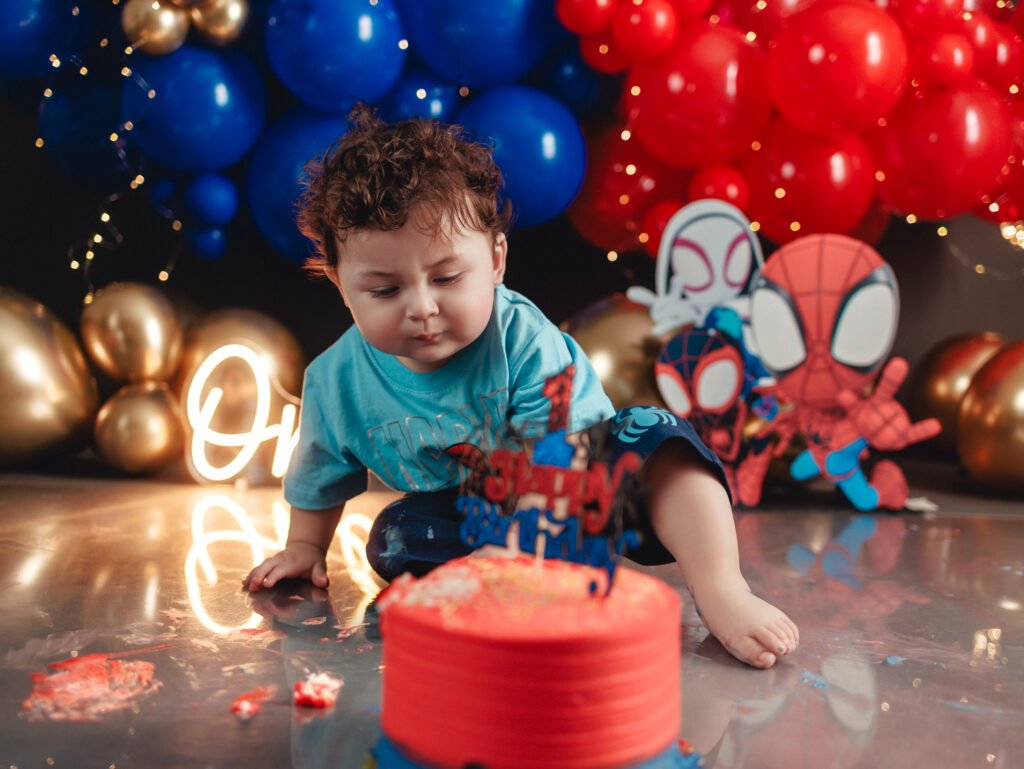 Adorable baby boy tasting his birthday cake during a Spider-Man Cake Smash Photography shoot.