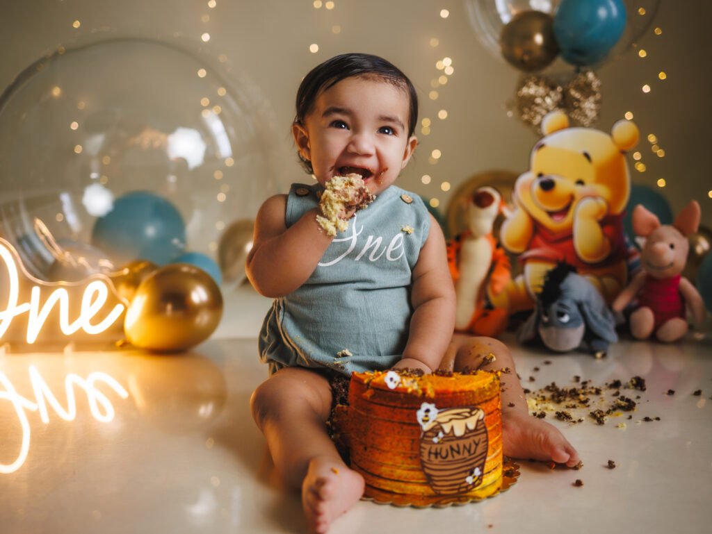 Smiling baby boy eating birthday cake with Winnie the Pooh backdrop, cinematic warm lighting in Beech Grove studio.